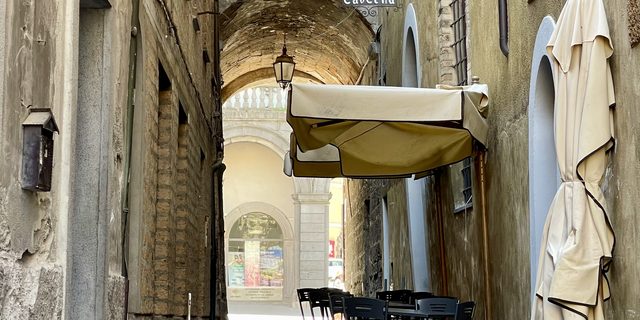 Stone alley in Italy with pizzeria sign and cafe tables under an archway